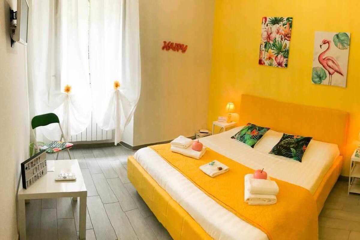 A bright yellow room with a bed, a chair, a table, and a mirror.