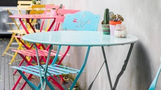 A row of colorful metal tables and chairs outside a building with a metal door and window shutters. - Alloggio Turistico Colosseo (Rome)