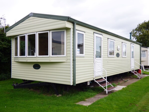 A single-story mobile home with a front porch, a small attached garage, and a set of stairs leading to the entrance. - Caravan Hire at Sunnydale Holiday Park (Louth)
