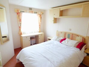 A bedroom with a bed, a desk, and a window with curtains. - Caravan Hire at Sunnydale Holiday Park (Louth)