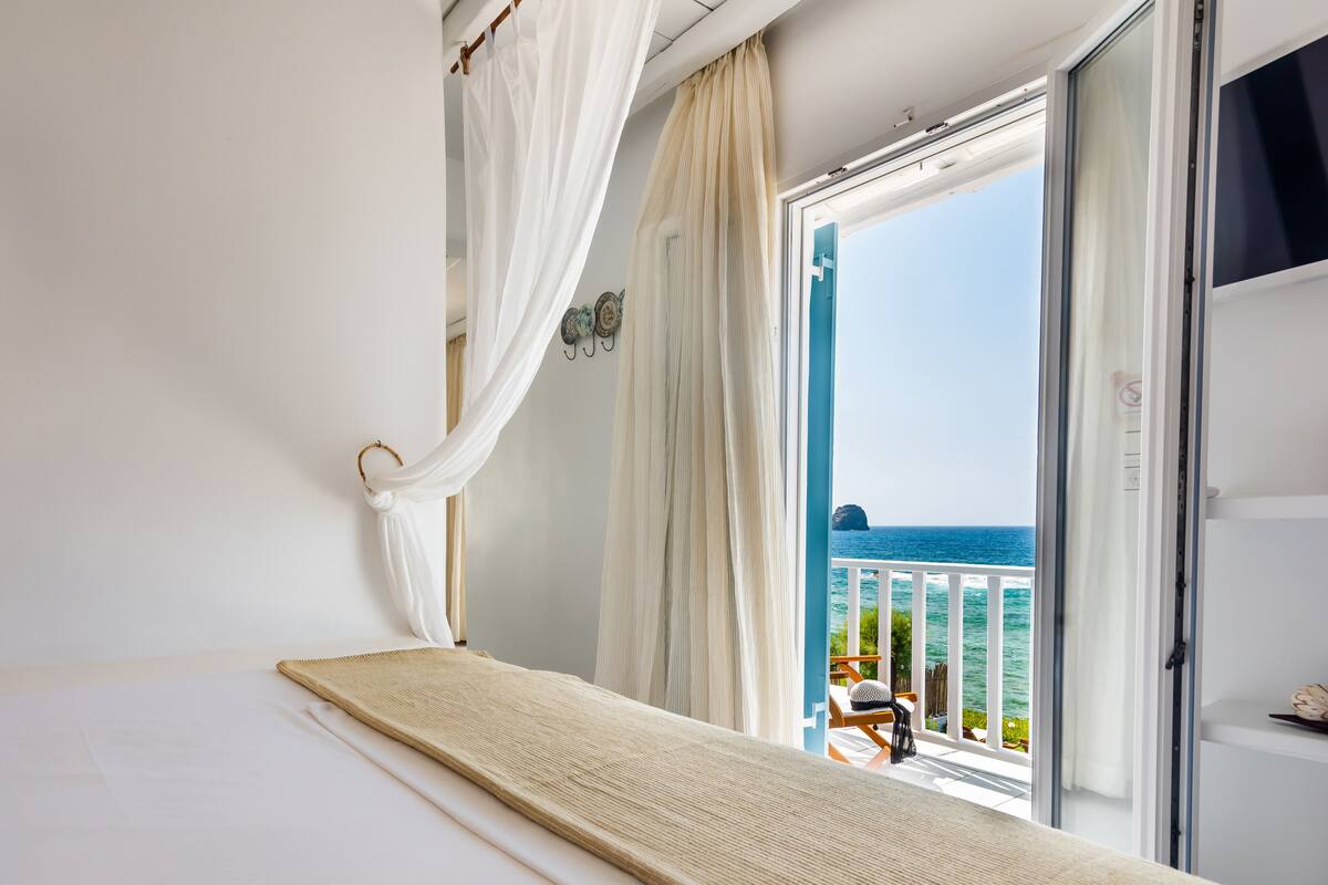 A bedroom with a bed, a view of the ocean, and a balcony with a chair.
