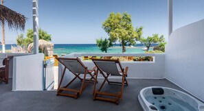 A balcony with two wooden chairs, a hot tub, and a view of the sea and beach. - Niki Savvas Studio & Suites (Milos)
