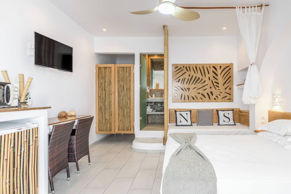 A modern hotel room with a bed, a desk, and a bathroom visible through an open door.