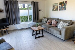 Un salon avec un canapé gris, une table basse, un téléviseur posé sur un meuble et un radiateur.