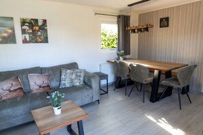 Een moderne woonkamer met een grijze bank, een houten salontafel en een eethoek met een houten tafel en grijze stoelen.