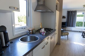 Une cuisine moderne dotée d’une cuisinière à gaz intégrée, d’un évier en acier inoxydable et d’une fenêtre laissant entrer la lumière naturelle.