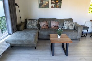 Ett modernt vardagsrum med en grå hörnsoffa, två dekorativa kuddar, ett litet träbord och en krukväxt.