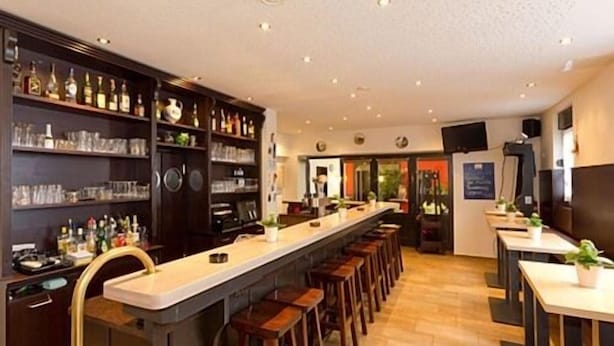 Eine Bar mit einer langen Theke, Hockern und Regalen voller Flaschen und Gläsern.