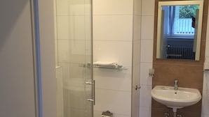 Ein modernes Badezimmer mit Duschkabine aus Glas, einem weißen Waschbecken und einem Spiegel darüber.