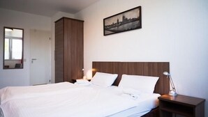 Ein Hotelzimmer mit einem großen Bett, einem hölzernen Kopfteil, zwei Nachttischen mit Lampen, einem gerahmten Stadtbild an der Wand und einer Tür links.