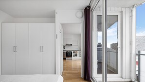 A modern bedroom with a large bed, a wardrobe, and a view of a kitchen and balcony through a glass door. - Siddis Apartment Sentrum 9 (Stavanger)