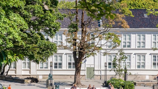 A serene park with a pond, benches, and a white building with a tiled roof in the background. - Siddis Apartment Sentrum 9 (Stavanger)