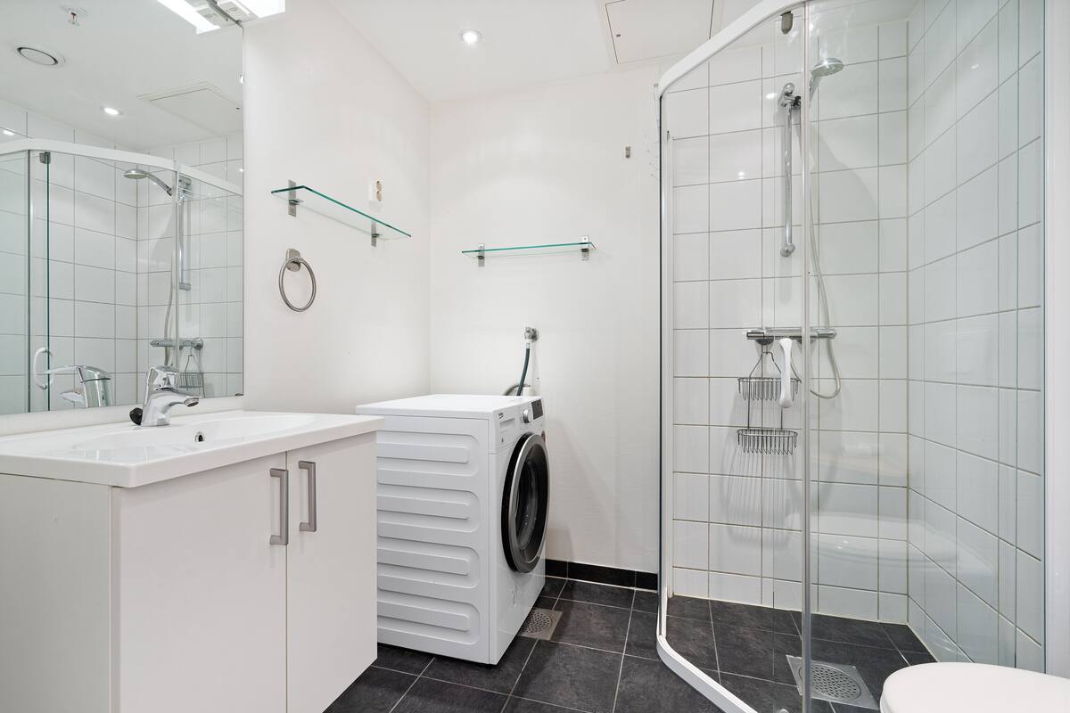 A modern bathroom with a glass-enclosed shower, a built-in washing machine, and a large mirror.