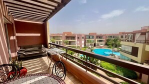 Un balcon aménagé avec un canapé, une table et une chaise, d’où l’on peut admirer une piscine et les bâtiments avoisinants.