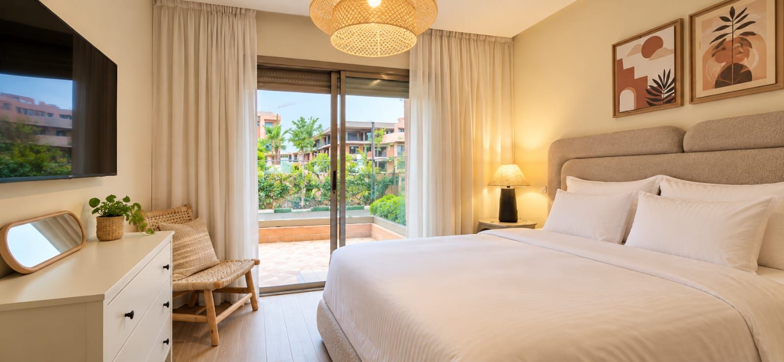 Una habitación de hotel con cama, escritorio, silla, lámpara y vistas al exterior.