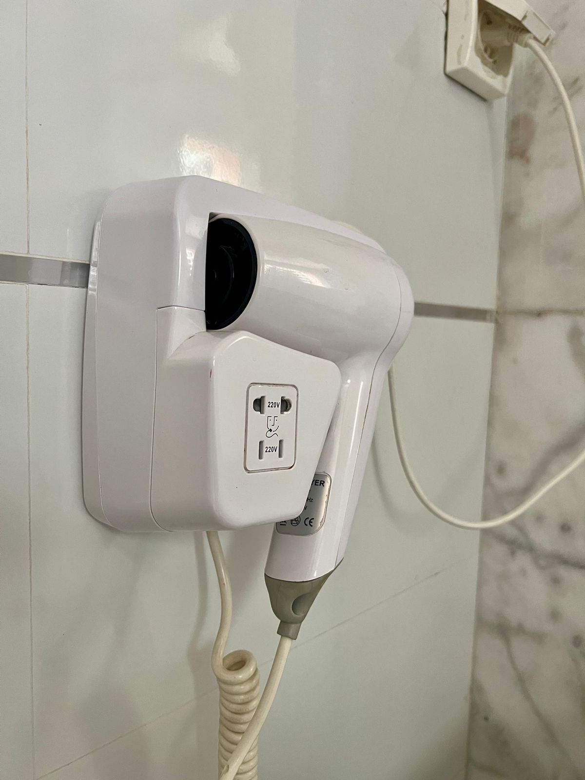 A hair dryer mounted on a tiled wall with a power cord.