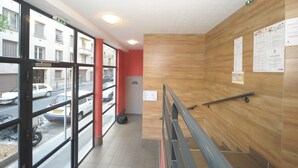 A hallway with wooden walls, a metal railing, and a view of parked cars through large windows. - Studilodge - Zola Park (Villeurbanne)