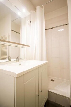 A bathroom with a white vanity, a mirror, a shower curtain, and tiled walls. - Studilodge - Zola Park (Villeurbanne)