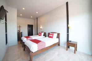 Habitación de hotel con dos camas, una mesita de noche, un televisor y una lámpara fijada a la pared.