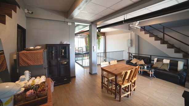 A spacious living area with a wooden dining table, black sofa, and a staircase leading to an upper floor. - OYO 465 Krung Kao Traveller Lodge (Ayutthaya)