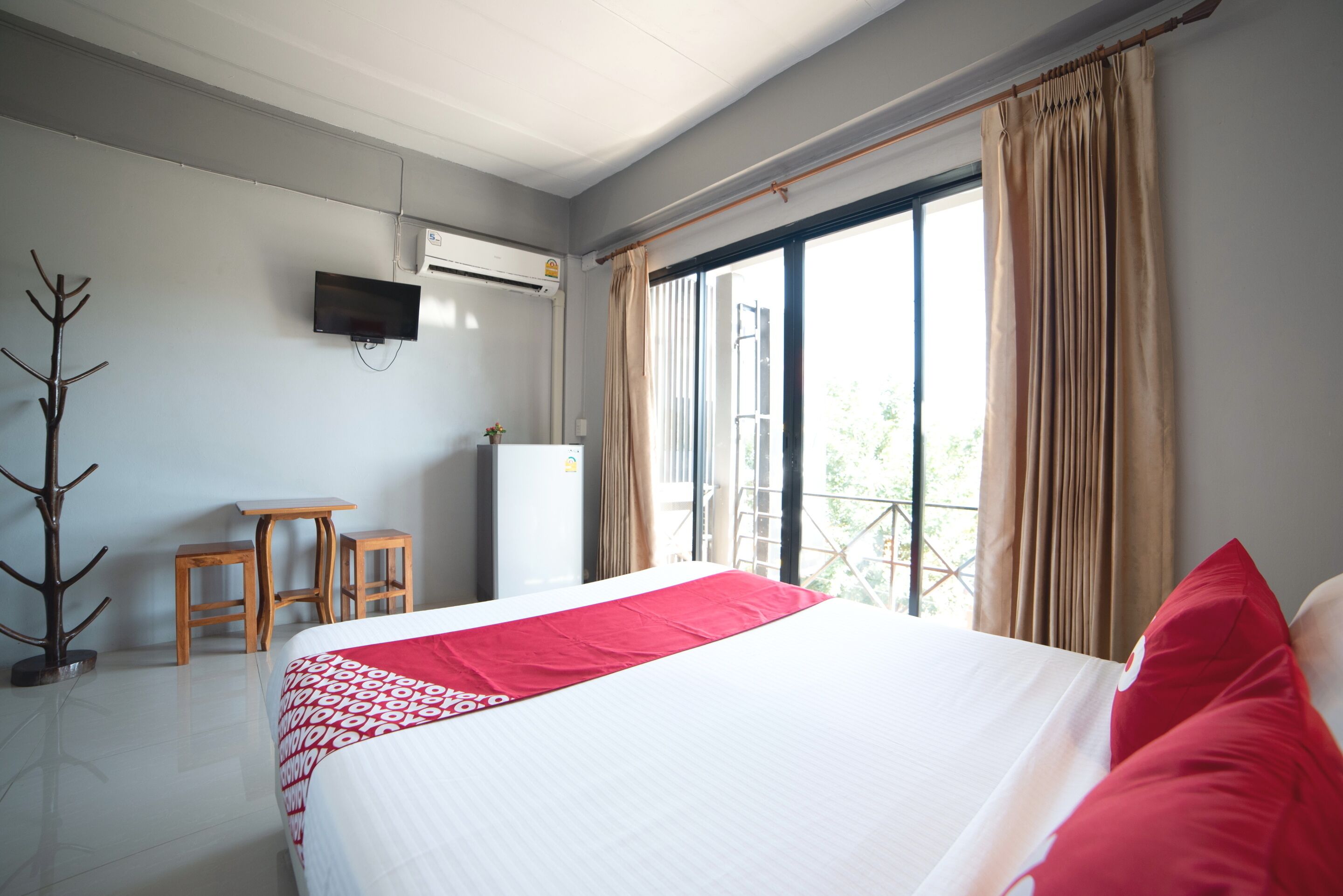 Una habitación de hotel con cama, televisión en la pared, ventana con cortinas y radiador.
