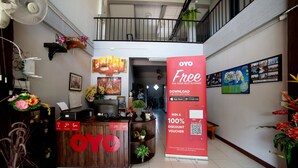 A hotel reception area with a wooden desk, a large 'OYO' sign, a promotional banner, and a view of the upper floor. - OYO 465 Krung Kao Traveller Lodge (Ayutthaya)