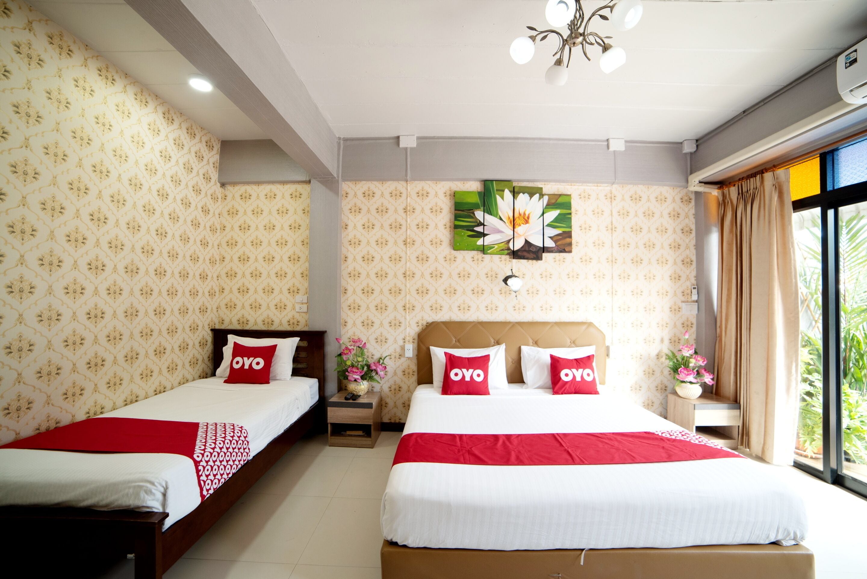 A hotel room with two beds, a large window, and a wall-mounted flower painting.