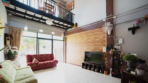 A spacious living area with a red sofa, a green sofa, a TV on a wooden stand, and a balcony with a railing. - OYO 465 Krung Kao Traveller Lodge (Ayutthaya)
