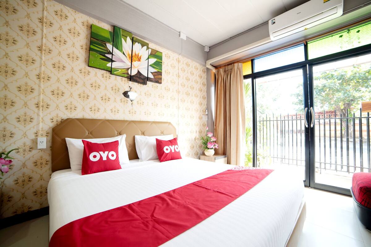 Une chambre d’hôtel avec un grand lit, une tête de lit, une fenêtre donnant sur un beau paysage et un mur orné d’un motif floral.