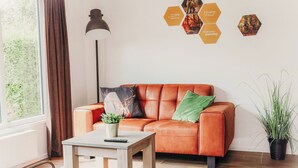 Een moderne woonkamer met een leren bank, een tafeltje met een plant, een vloerlamp en een wanddecoratie van hexagonen.