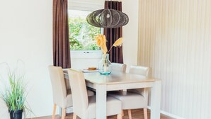 Een eetruimte met een houten tafel, vier stoelen, een hanglamp en een raam met gordijnen.