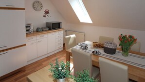 Une cuisine avec des meubles blancs, un four à micro-ondes et une table à manger avec des chaises. Il y a une horloge au mur et une fenêtre au-dessus de la table.