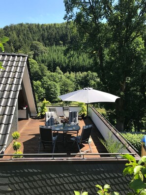 Una terraza en la azotea con mesa, sillas y sombrilla.