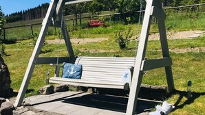 Une balançoire en bois avec un banc en dessous, entourée d’escaliers en pierre et d’un champ d’herbe.