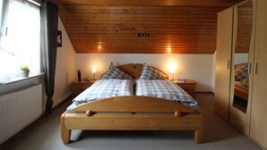 Un plafond en bois sur lequel on peut lire les mots « Traume Zelt », un lit avec une literie à carreaux, dans une pièce aux murs en bois et une fenêtre ornée de rideaux.