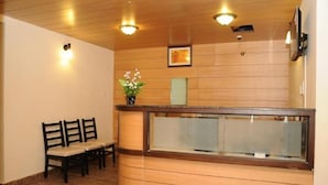 A reception area with wooden paneling, a reception desk, two chairs, and a vase with flowers. - Balaji Residency (Chennai)