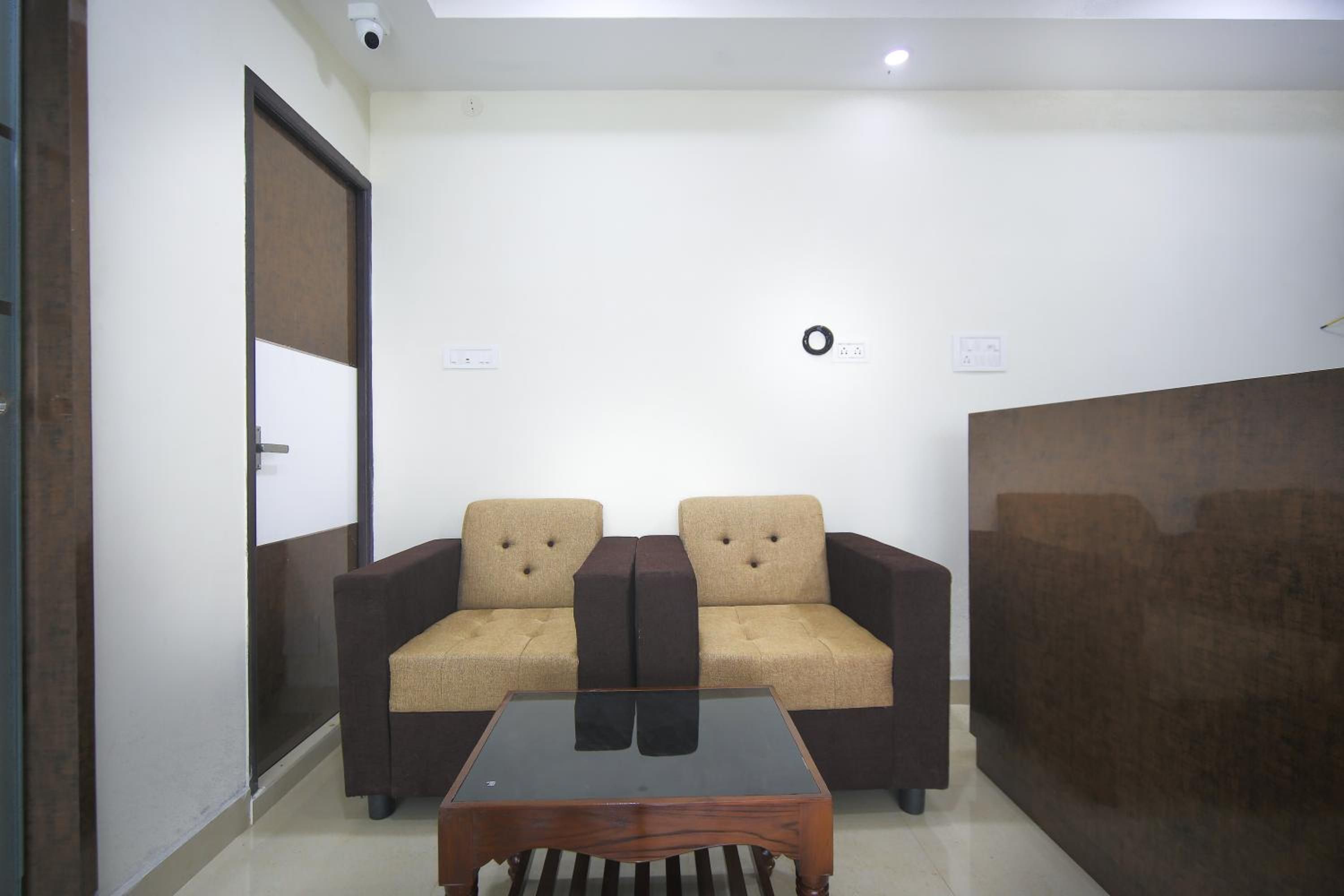 A room with two sofas, a glass-top coffee table, a door, and a wall-mounted light fixture.