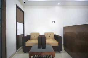 A room with two sofas, a glass-top coffee table, a door, and a wall-mounted light fixture. - Balaji Residency (Chennai)