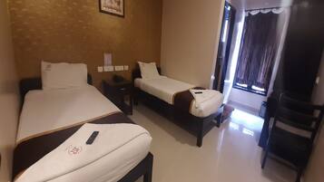 Quarto de hotel com duas camas de solteiro, uma mesinha, uma cadeira e uma televisão.