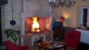 A cozy living room with a stone fireplace, a red armchair, a wooden coffee table with books, and a television. - Le Bourg d'Aunou (Aunou-sur-Orne)