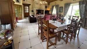 A spacious living area with a fireplace, wooden dining table, and a kitchen in the background. - Le Bourg d'Aunou (Aunou-sur-Orne)