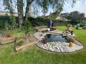 Een tuin met een vijver, een houten terras en diverse planten.