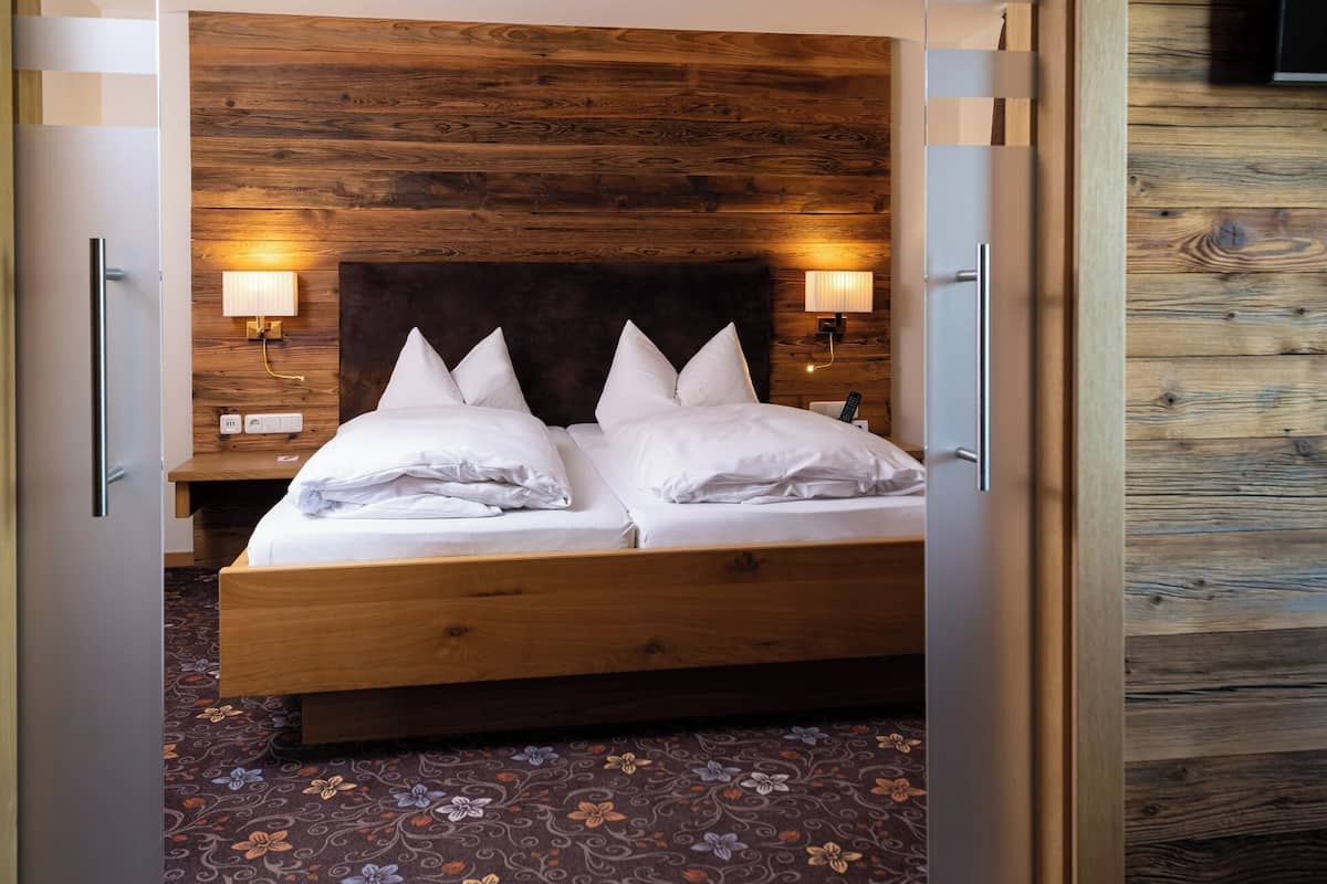 A double bed with white linens, two bedside lamps, and a wooden headboard.