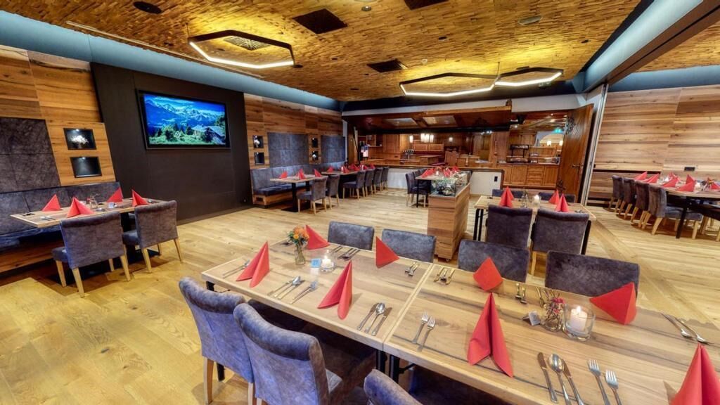A restaurant with multiple dining tables, each set with cutlery and napkins, and a large screen displaying a scenic view.