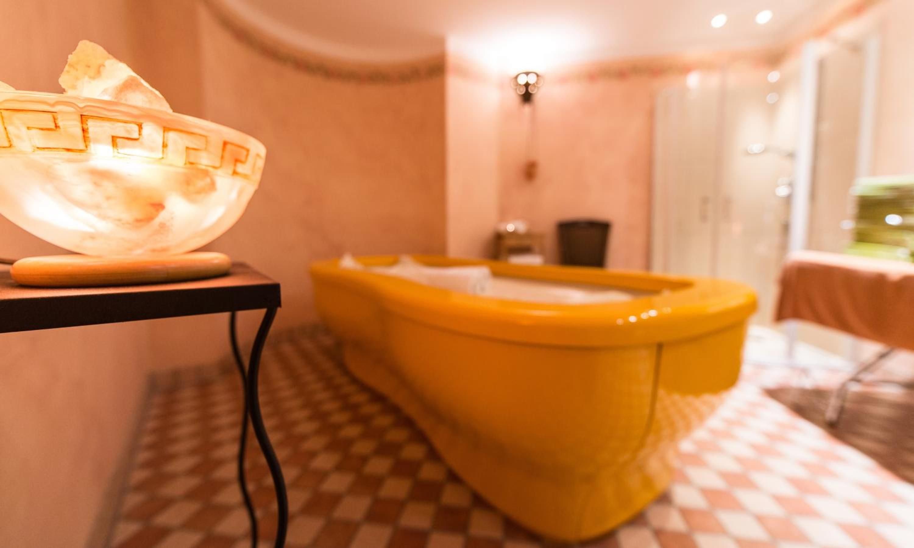 Un baño con piso a cuadros, una bañera amarilla y un accesorio de iluminación en la pared.