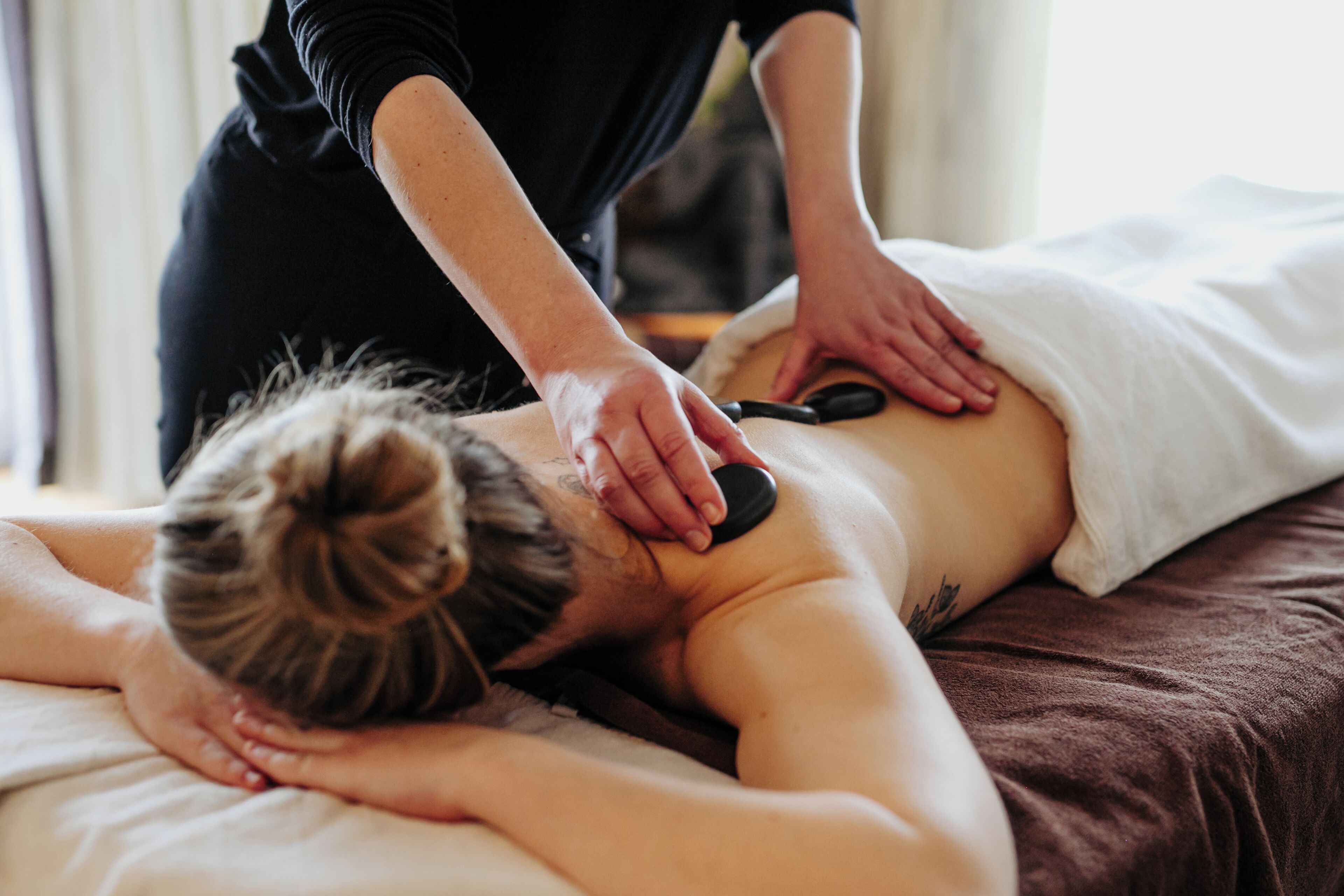 A person receiving a back massage on a bed with a white towel and a brown blanket.