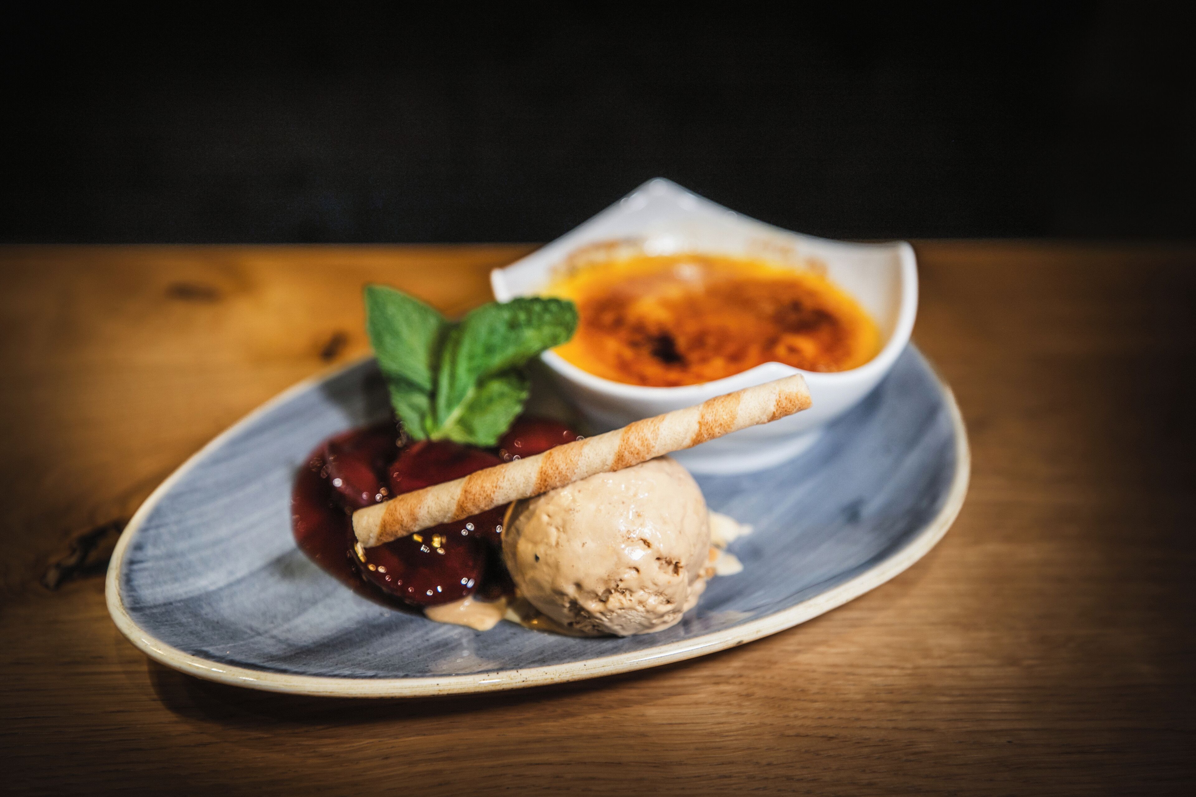 Un plato de postre con helado, compota de bayas y una galleta.