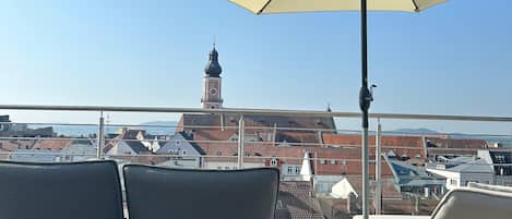 A rooftop terrace with two grey cushioned chairs and a large beige umbrella.