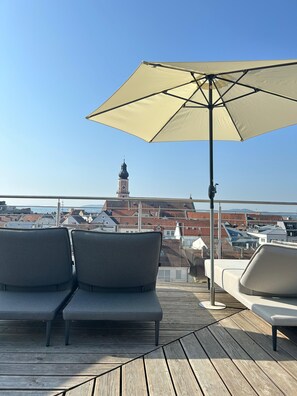 A rooftop terrace with two grey cushioned chairs and a large beige umbrella. - Hotel Randsbergerhof (Cham)