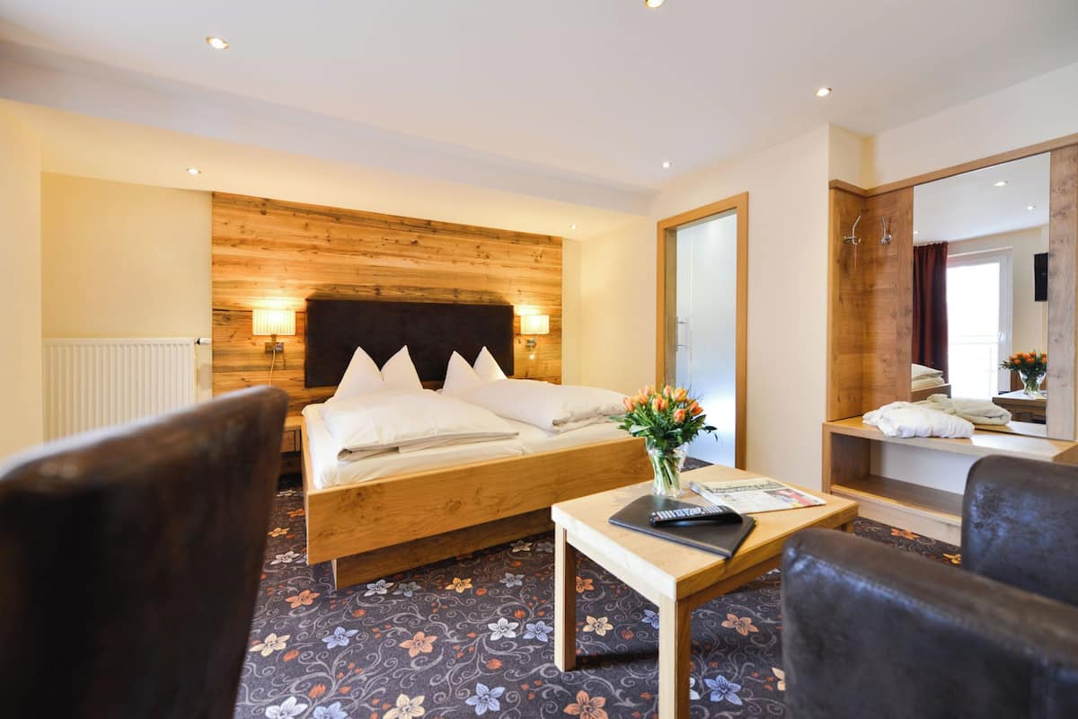 A hotel room with a wooden headboard bed, a small table with a laptop, a chair, and a large mirror.